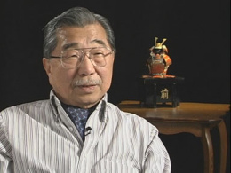 Gordon Hirabayashi. HE is wearing a collared shirt and has on glasses. He has medium, coifed hair and a thin moustache.
